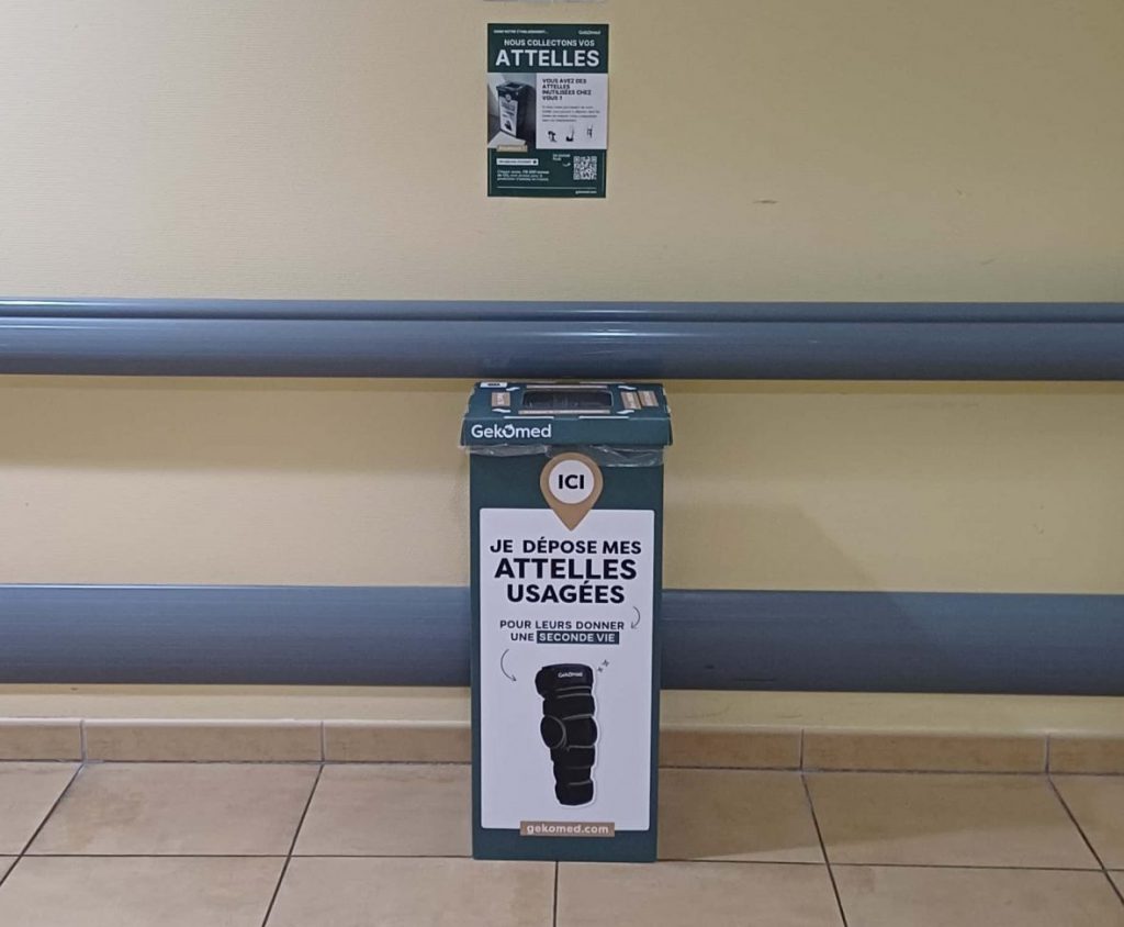 Borne de collecte d’attelles usagées Gekomed installée dans un couloir d’hôpital, sous une signalétique indiquant les services de rééducation.